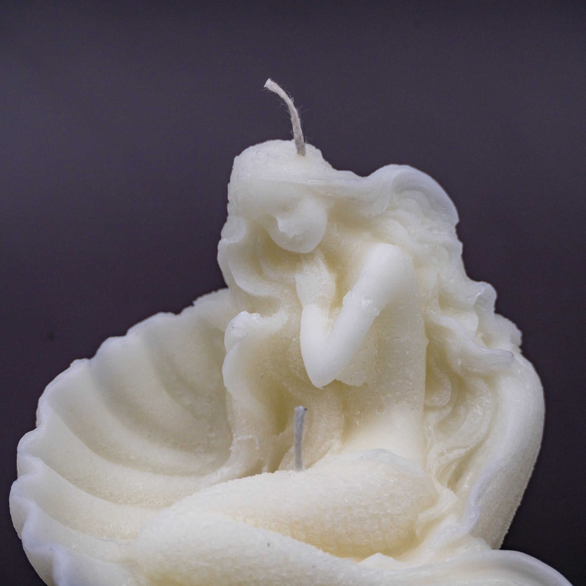 The candle features an intricate, whimsical sculpture of a serene mermaid nestled in or wrapped around a spiral seashell, designed to add a serene, romantic, storybook or coastal charm to any space.