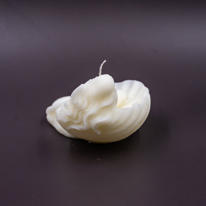 The candle features an intricate, whimsical sculpture of a serene mermaid nestled in or wrapped around a spiral seashell, designed to add a serene, romantic, storybook or coastal charm to any space.