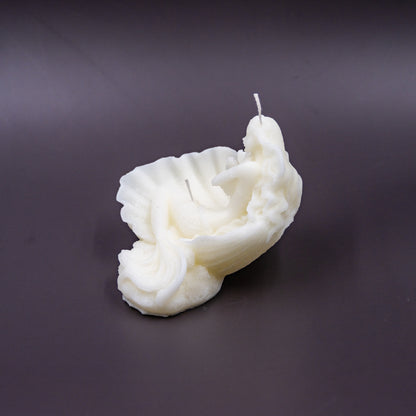 The candle features an intricate, whimsical sculpture of a serene mermaid nestled in or wrapped around a spiral seashell, designed to add a serene, romantic, storybook or coastal charm to any space.