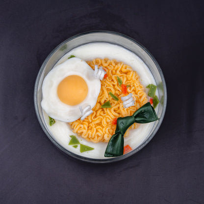 This highly realistic, handcrafted candle is a culinary work of art, designed to perfectly mimic a bowl of ramen noodles with a poached egg, kelp knot, carrots, and other vegetable toppings, all in a white savory bone broth base. Primarily made from a blend of natural soy and beeswax, this unique item is an ideal novelty decor piece. The entire assembly is presented in a glass jar with rose golden lid.