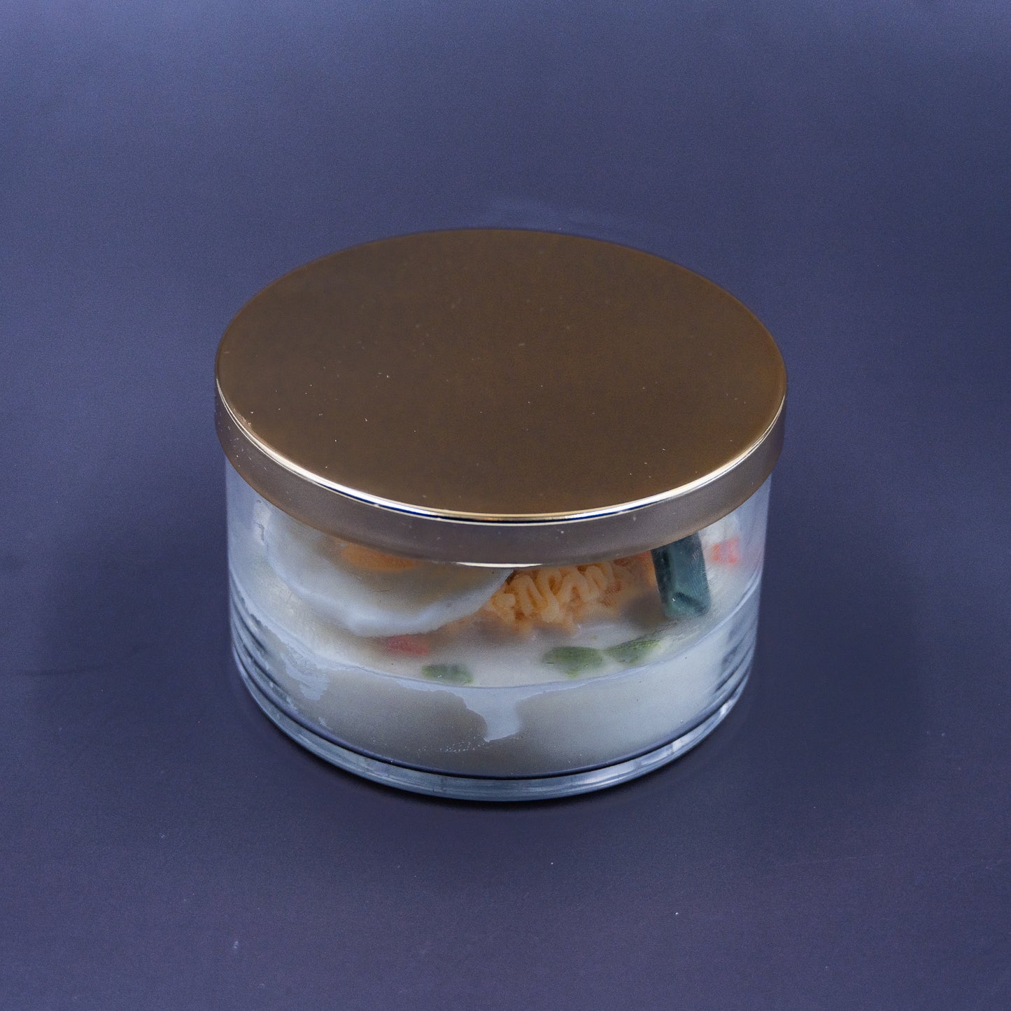 This highly realistic, handcrafted candle is a culinary work of art, designed to perfectly mimic a bowl of ramen noodles with a poached egg, kelp knot, carrots, and other vegetable toppings, all in a white savory bone broth base. Primarily made from a blend of natural soy and beeswax, this unique item is an ideal novelty decor piece. The entire assembly is presented in a glass jar with rose golden lid.